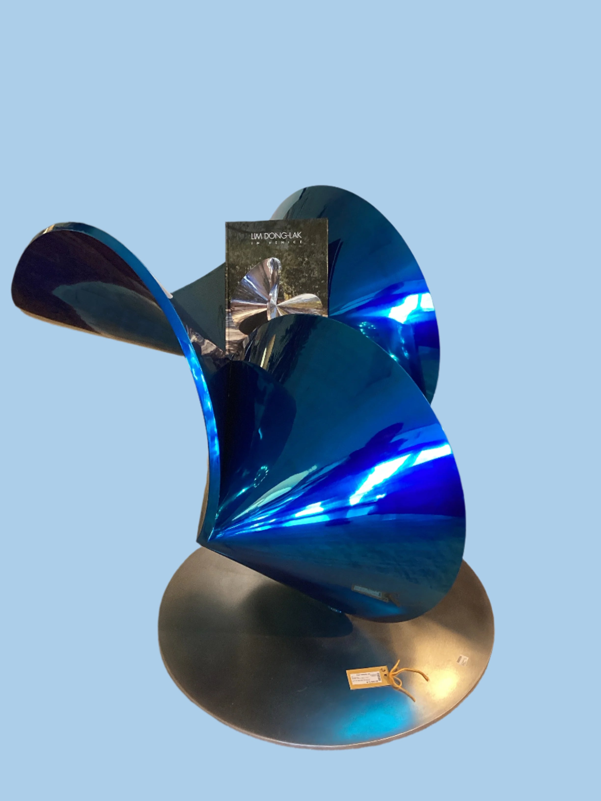 A modern blue bird sculpture with outstretched wings, made of metal, placed on a circular base.