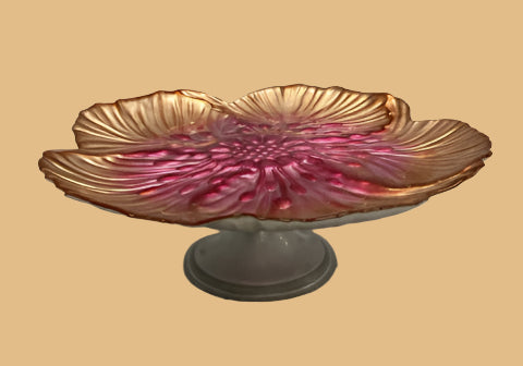 Decorative glass bowl with pink interior and gold exterior on a white pedestal against a gray background