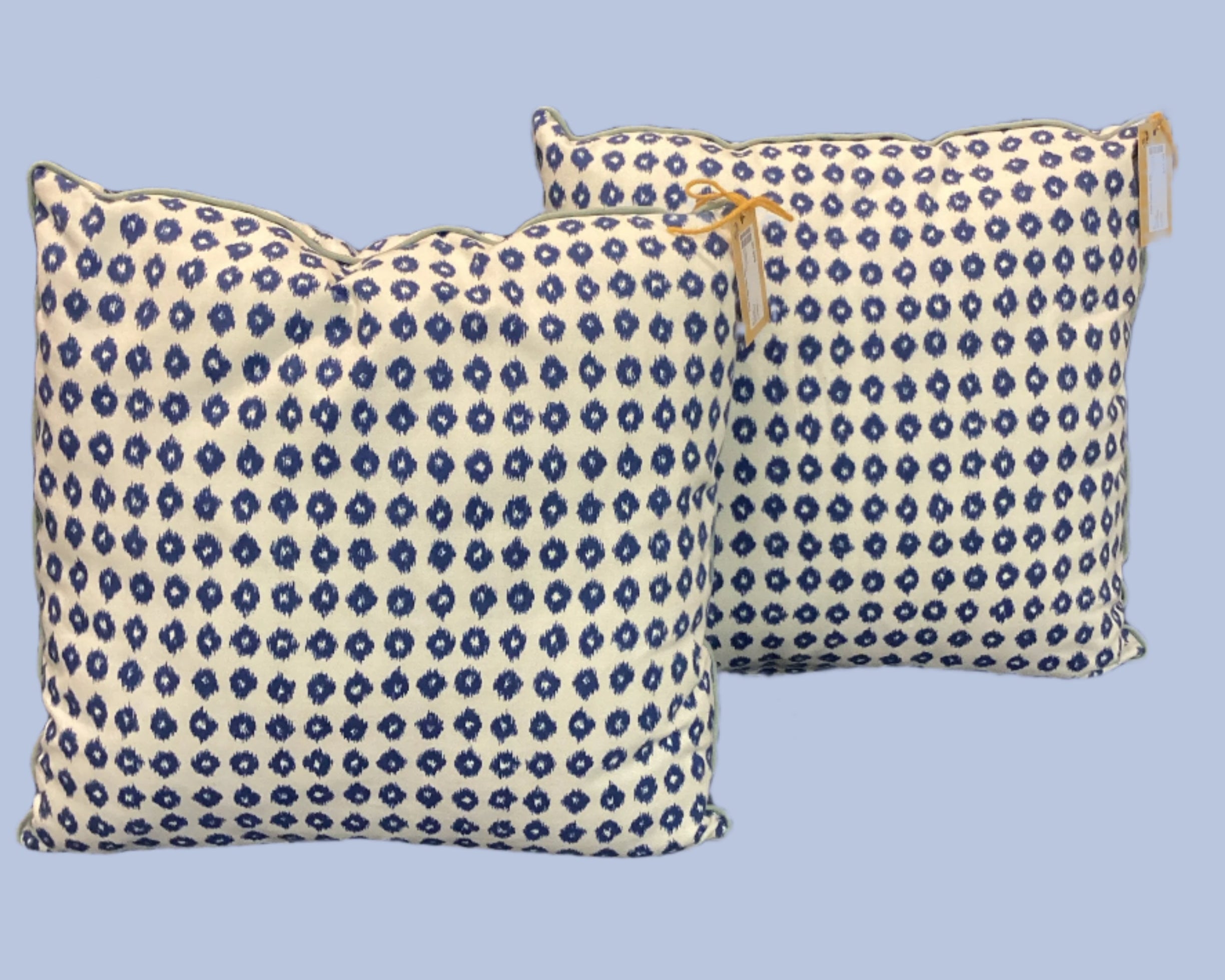 Two square blue pillows with a geometric pattern, placed on a blue sofa, with a close-up on the pillows showing the detail of the pattern and a tag visible.
