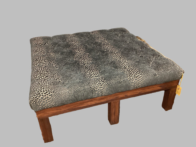A large square ottoman with a tufted chenille fabric in a patterned color, placed on a patterned rug.